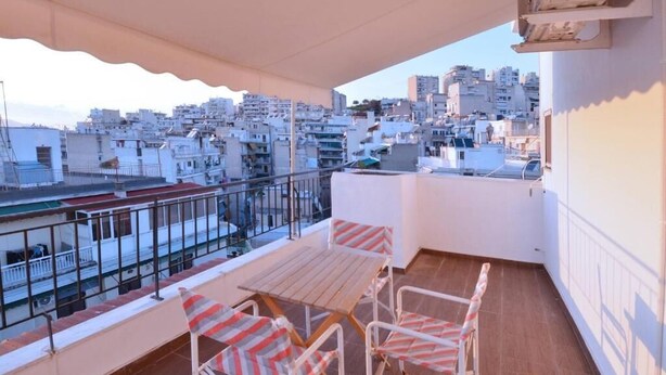 A balcony with a table and chairs, overlooking a cityscape.
