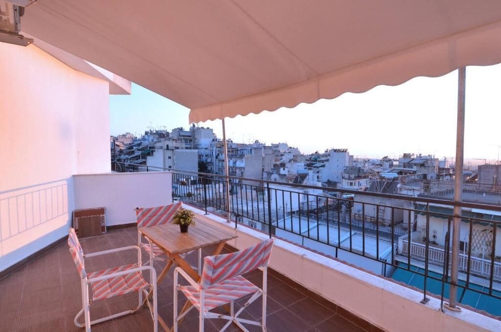 A balcony with a table and chairs, a view of the cityscape, and a pool in the background.