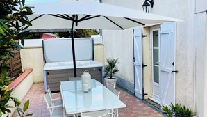 Een terras met een glazen tafel en stoelen, een witte parasol en een bloempot met plant.
