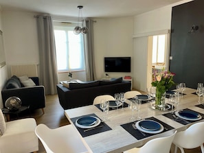 A modern living room with a dining area, a flat-screen TV, and a sofa.