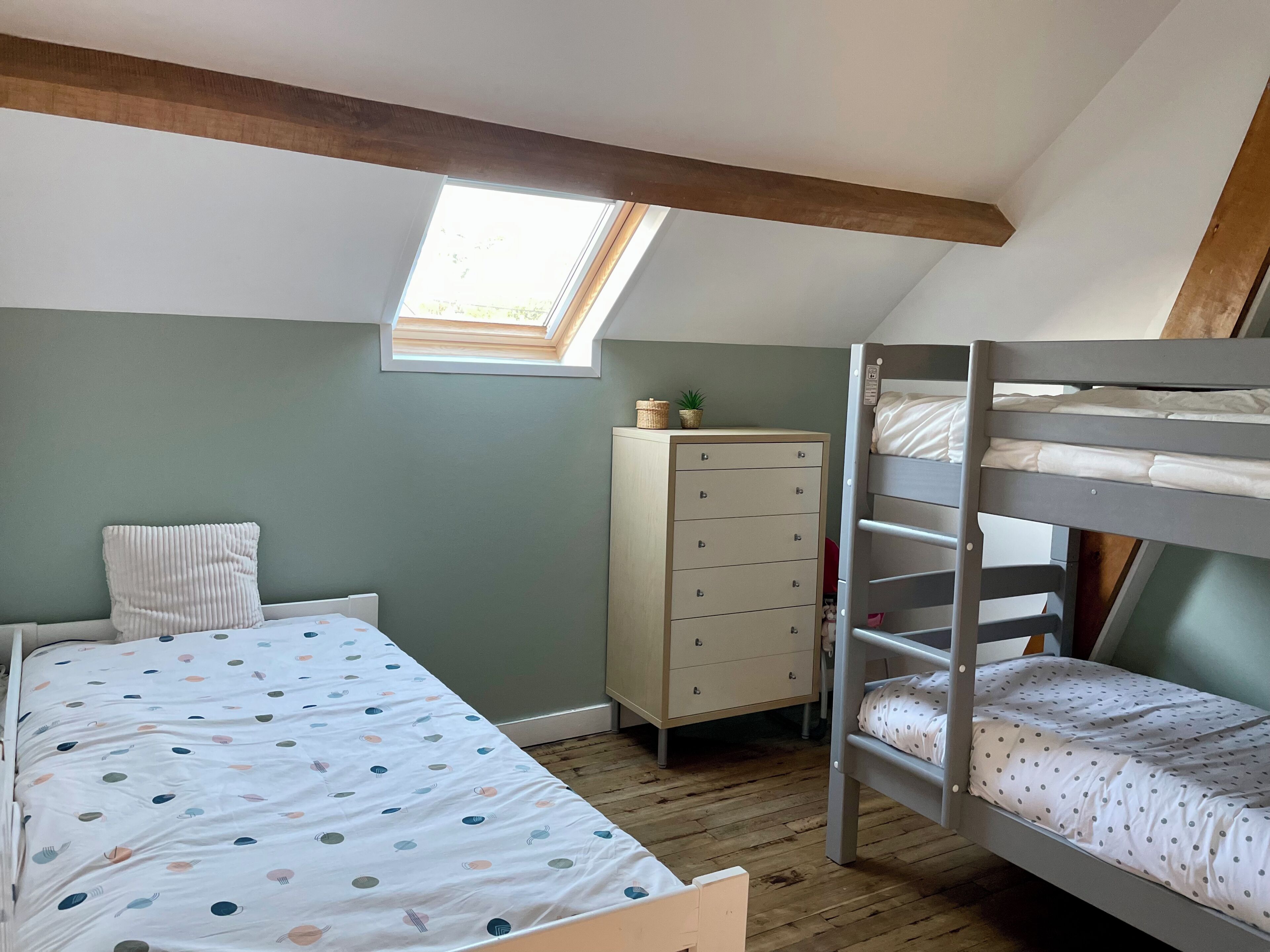 Een slaapkamer met een stapelbed, een dressoir, een raam en een dakraam.