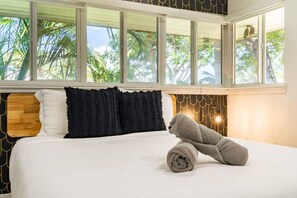 A bedroom with a bed, pillows, a teddy bear, and large windows with a view of palm trees. - Waterfront Fun! 6BR • Pool • Beach 5 Min (Hollywood)