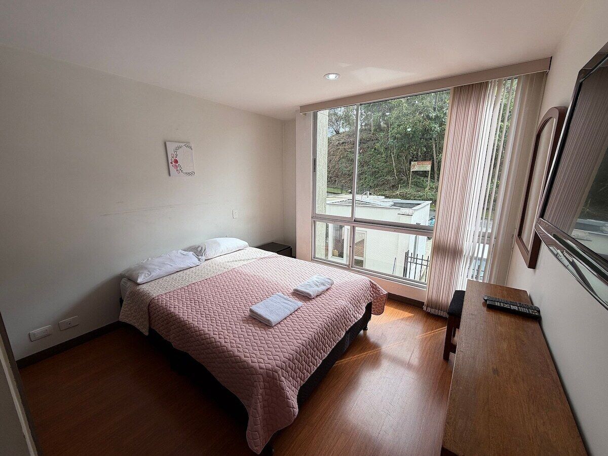 Ein Schlafzimmer mit einem Bett, einem Fenster, Holzboden und einem Fernseher.
