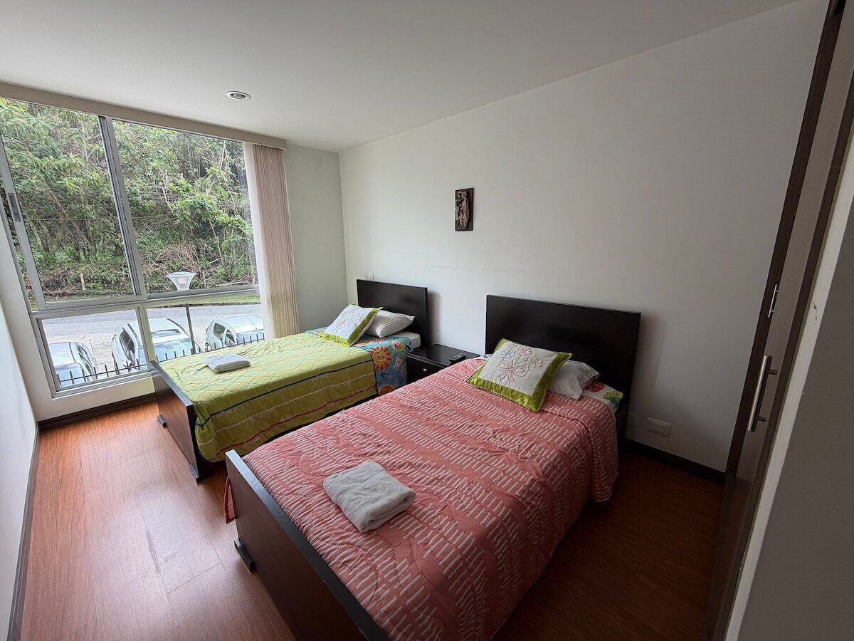 Ein Hotelzimmer mit zwei Betten, einem Fenster mit Blick auf Grünflächen und einem kleinen Tisch mit Stühlen draußen.