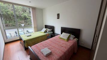 Une chambre d’hôtel avec deux lits, une fenêtre donnant sur un espace verdoyant et une petite table avec des chaises à l’extérieur.
