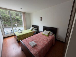 Quarto de hotel com duas camas, janela com vista para áreas verdes e uma pequena mesa com cadeiras do lado de fora.