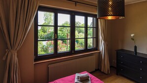 Une chambre avec une grande fenêtre, un radiateur, un lit avec des serviettes, une commode et une lampe suspendue.