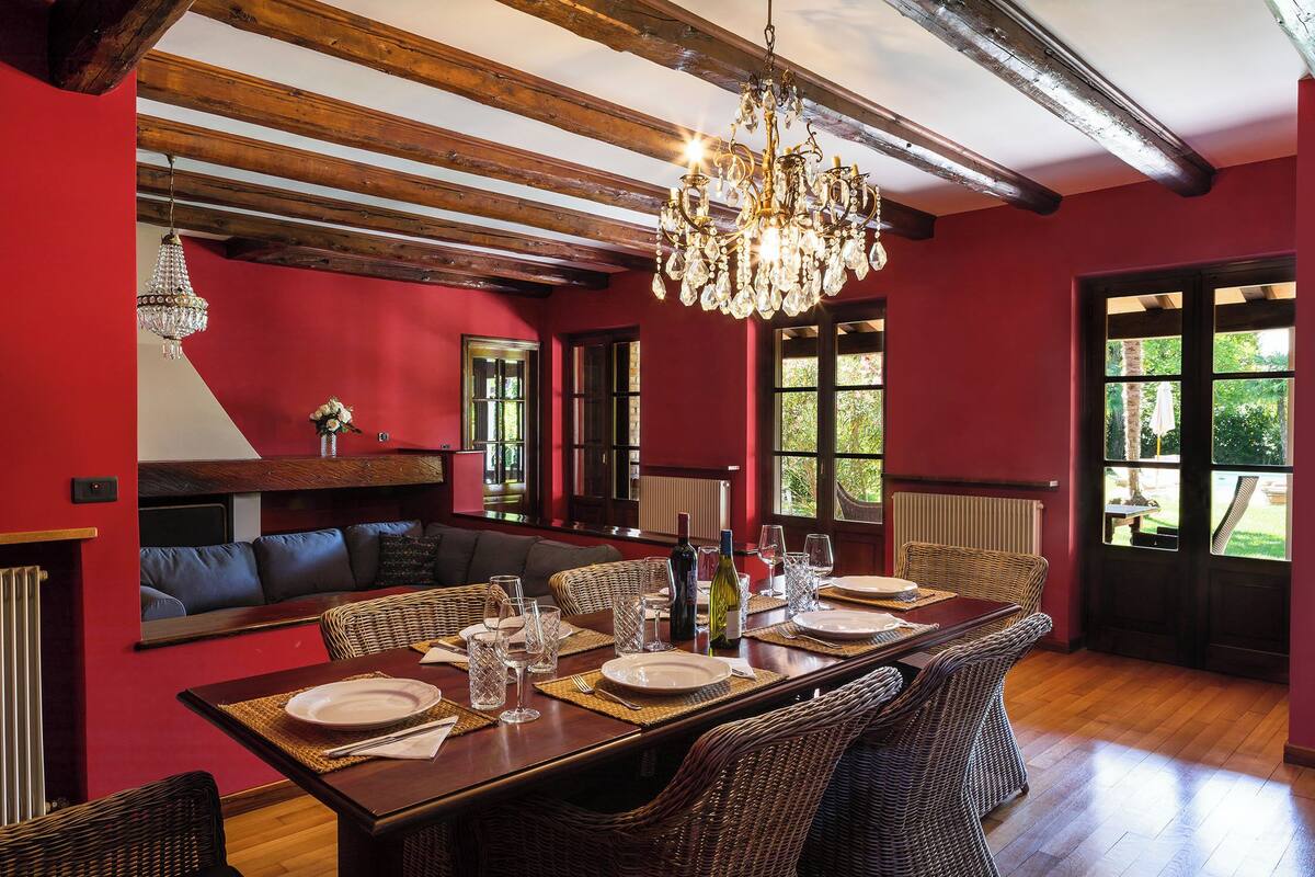 A dining area with a long table, wicker chairs, and a chandelier.