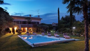 Une piscine avec des chaises longues, une maison avec un toit en tuiles et une végétation luxuriante tout autour.