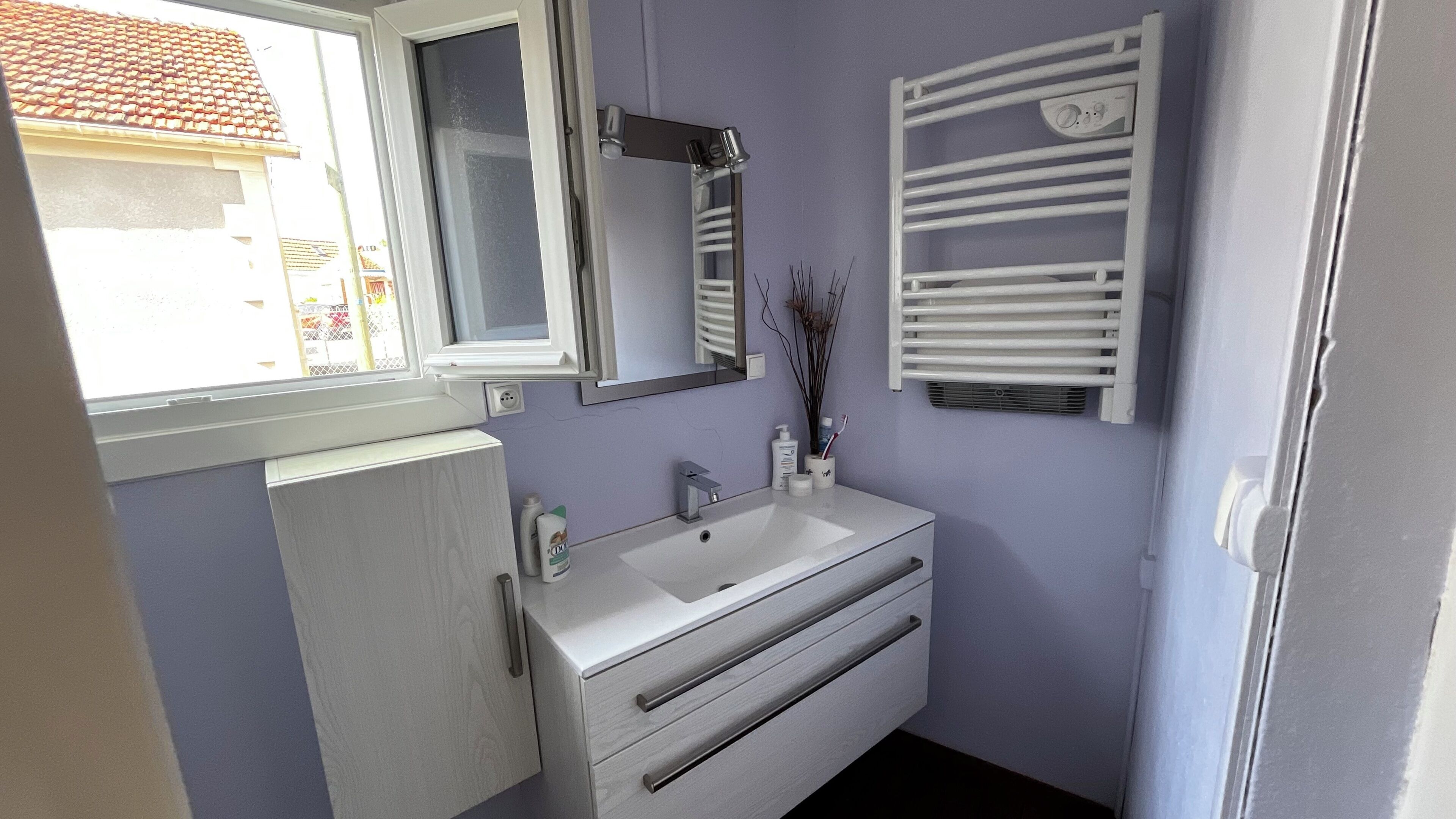 Un baño con lavamanos blanco, espejo y toallero.