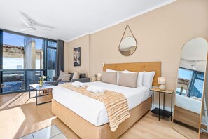 Une chambre d’hôtel moderne dotée d’un grand lit, d’un canapé, d’une petite table, d’un miroir et d’un balcon avec vue.