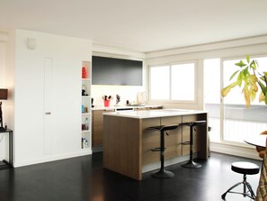 A modern kitchen with a central island, bar stools, a window with a view, and a door leading to another room. - Apartment on the 31st floor with balcony in PARIS (Paris)