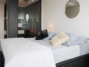 A modern bedroom with a large bed, a round mirror, and a bathroom visible through an open door. - Apartment on the 31st floor with balcony in PARIS (Paris)