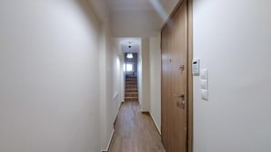Een smalle gang met houten vloeren, een houten deur aan de rechterkant, en een lichtschakelaar op de muur.