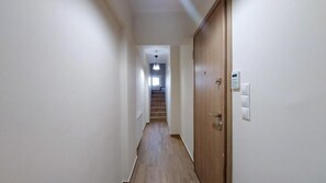 Ein schmaler Flur mit Holzboden, einer Holztür rechts und einem Lichtschalter an der Wand.