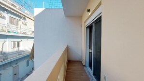 Een smal balkon met een houten vloer, een witte muur en een schuifglazen deur.