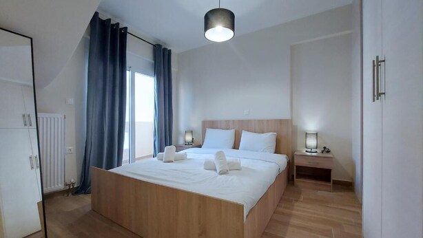 Een moderne slaapkamer met een houten bed, een nachtkastje met een lamp, een radiator en een raam met gordijnen.