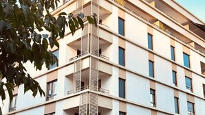 Een meerlaags hotel met een modern design, voorzien van balkons op elke verdieping, een parkeerplaats ervoor en een heldere lucht.