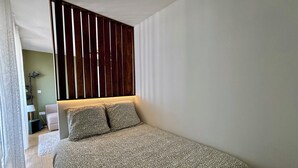 Een slaapkamer met een bed, een lattenwand, een nachtkastje en een lamp.