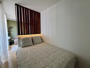 A bedroom with a bed, a wooden slat partition, a nightstand, and a lamp. - Schiltigheim: 6th Floor Studio with Terrace (Schiltigheim)