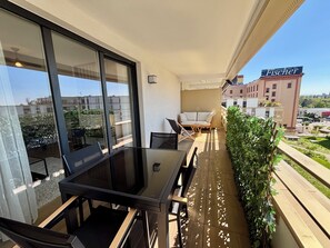 A balcony with a table and chairs, a potted plant, and a view of a building with a sign. - Schiltigheim: 6th Floor Studio with Terrace (Schiltigheim)