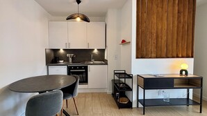 Een moderne keuken met witte kasten, een eettafel met stoelen, een zwart metalen bijzettafeltje en een houten vloer.