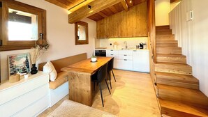 A modern kitchen with wooden cabinets, a dining area with a wooden table, and a staircase. - Charming studio with mountain view & balcony (Combloux)