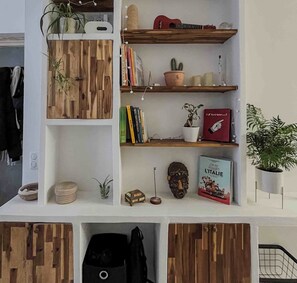 A room with a white wall, wooden shelves, a small plant, a guitar, books, and a decorative mask. - 70 m² apartment with terrace in the heart of Paris (Paris)