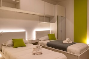Ein modernes Hotelzimmer mit zwei Betten, einem Nachttisch, einem Spiegel und integrierten Schränken.