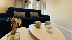 Een woonkamer met een donkerblauwe bank, twee gestreepte kussens, een witte salontafel met twee mokken en een glazen pot, en een vaas met gedroogde bloemen.
