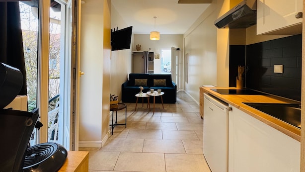 Een moderne keuken met een inbouwoven, een zithoek met een bank en tafel, en een hal die naar een woonkamer leidt.