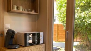 Een compacte keuken met een magnetron, koffiezetapparaat en een houten kastje met een ruitpatroon.