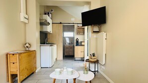 Een knus woongedeelte met een kitchenette, een flatscreen televisie aan de muur en een eethoek met twee tafels.
