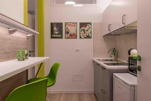 Cozinha compacta com pia, micro-ondas e cadeiras verdes.