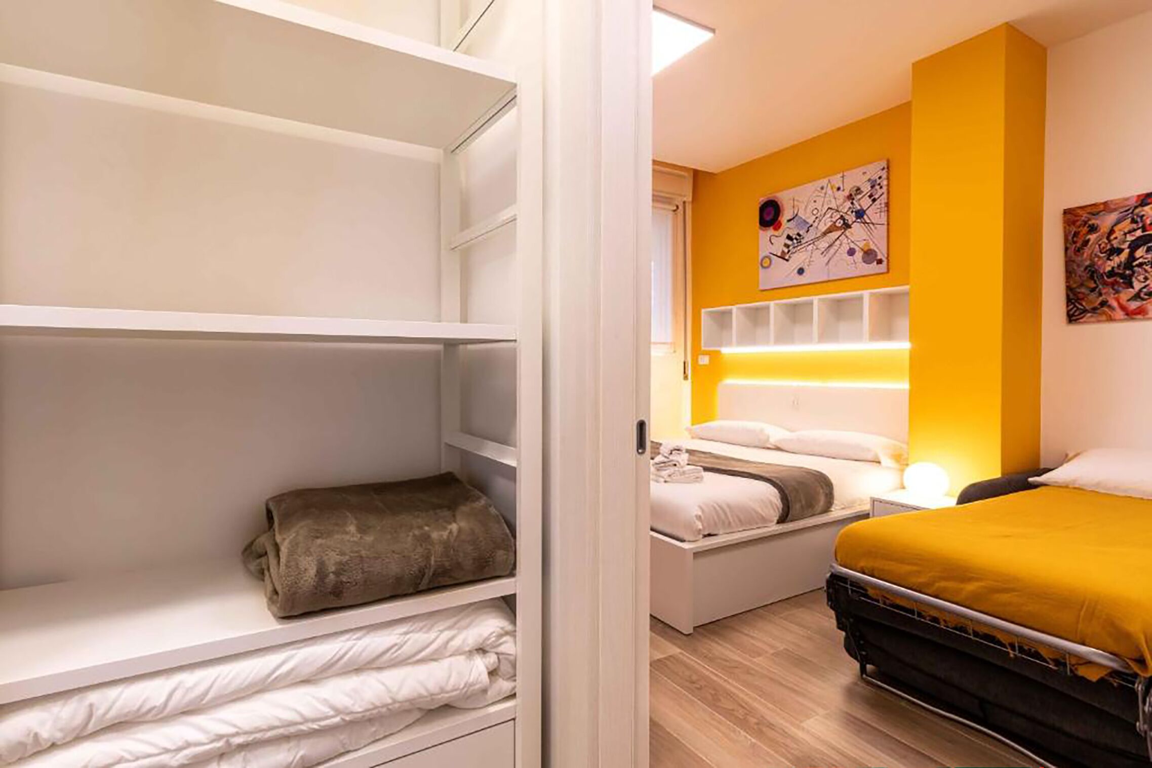 Una habitación de hotel con cama, mesita de noche, armario y una pared decorada con obras de arte.