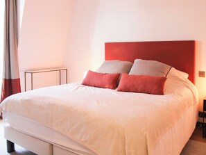 Un lit avec un matelas blanc et des oreillers rouges et beige, une table de chevet et une tête de lit rouge.