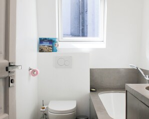 Une salle de bain avec des toilettes, une baignoire, une fenêtre et un magazine accroché au mur.