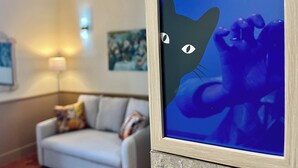 Una obra de arte enmarcada con el rostro de un gato en una pared, un sofá y una lámpara en una habitación.