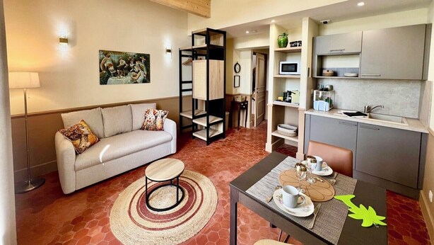 Una sala de estar con sofá, una mesita redonda y una cocina con armarios y microondas.