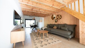 Ein modernes Wohnzimmer mit Holzboden, einer Couch, einem Couchtisch und einem an der Wand montierten Fernseher.