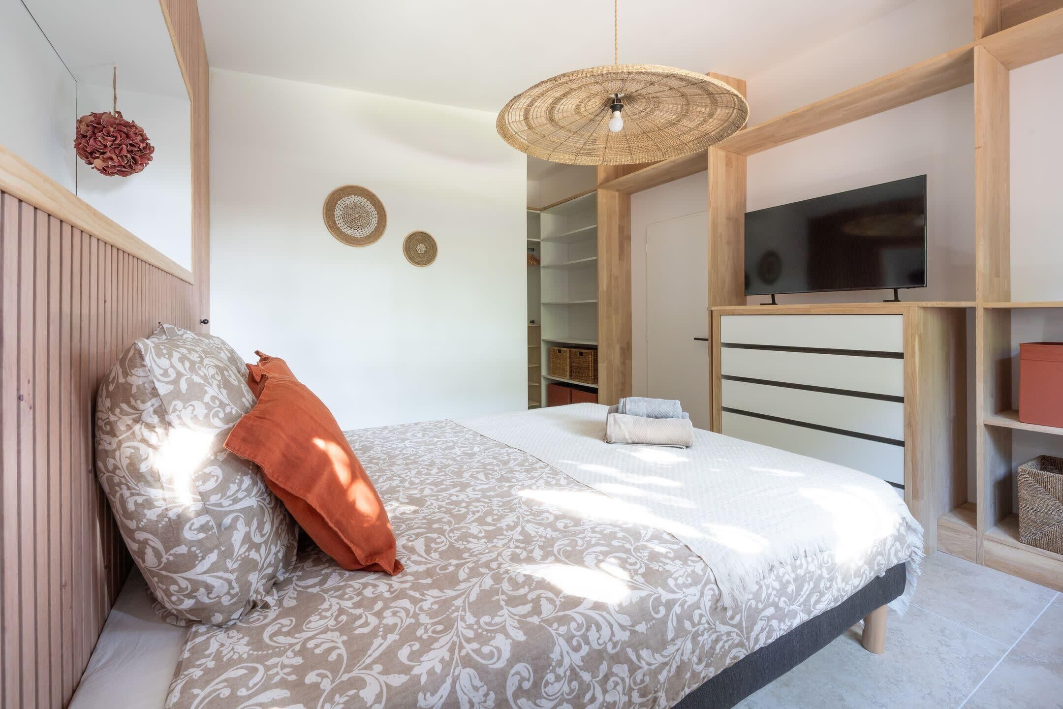 Une chambre à coucher comprenant un lit, une télévision, une armoire et un luminaire suspendu.