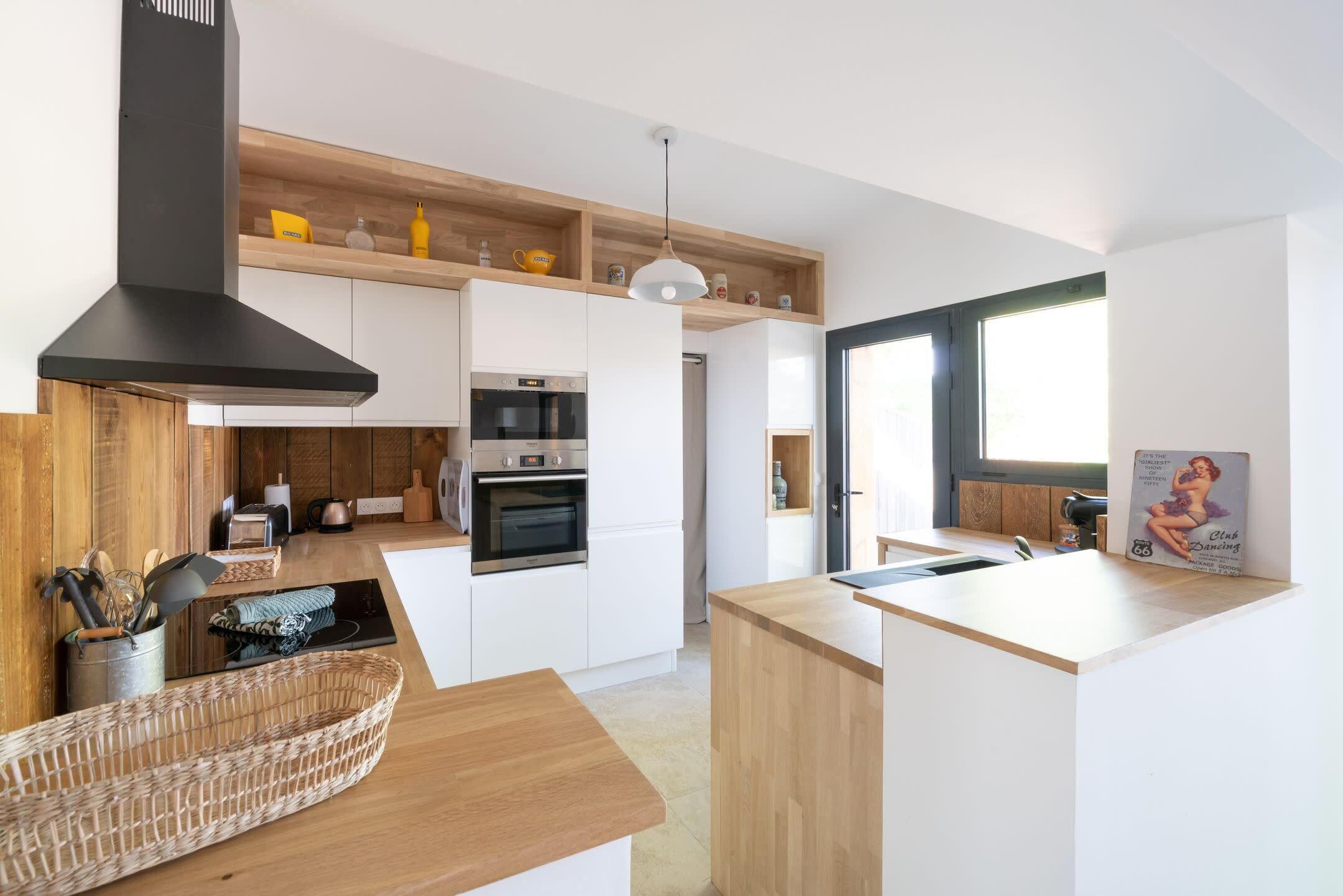 Una cocina moderna con armarios blancos, una campana extractora negra y estantes de madera.
