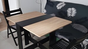 Una habitación con un sofá negro que tiene diseños de hojas blancas, una mesa de madera y dos sillas negras.