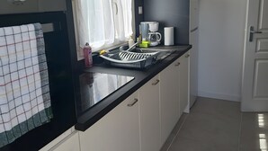 Una cocina moderna con encimera negra, escurreplatos, cafetera y ventana con cortinas.