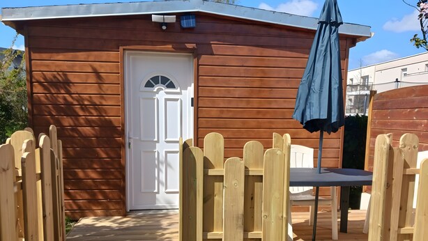 Una cabaña de madera con puerta blanca, un pequeño porche y un paraguas azul.