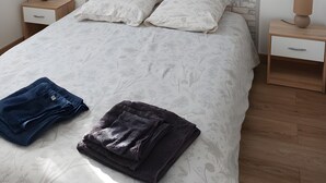 Una cama bien hecha con una colcha estampada, dos almohadas y toallas dobladas. Hay dos mesitas de noche con lámparas, un armario y un cabecero con diseño de ladrillo.