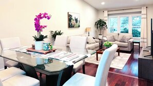 A modern living room with a glass dining table, white sofas, a coffee table, and a TV.