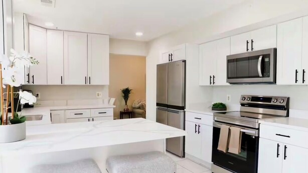 A modern kitchen with white cabinets, a central island with stools, a refrigerator, a microwave, and an oven.