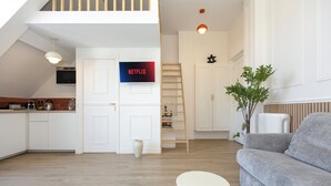 Ein moderner Wohnraum mit Küche, einer Treppe, einer Couch und einem Fernseher, der 'NETFLIX' anzeigt.