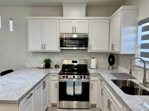 A kitchen with white cabinets, a stainless steel stove, a microwave, and a sink. - Cardinal Home - Family Friendly (Mission)